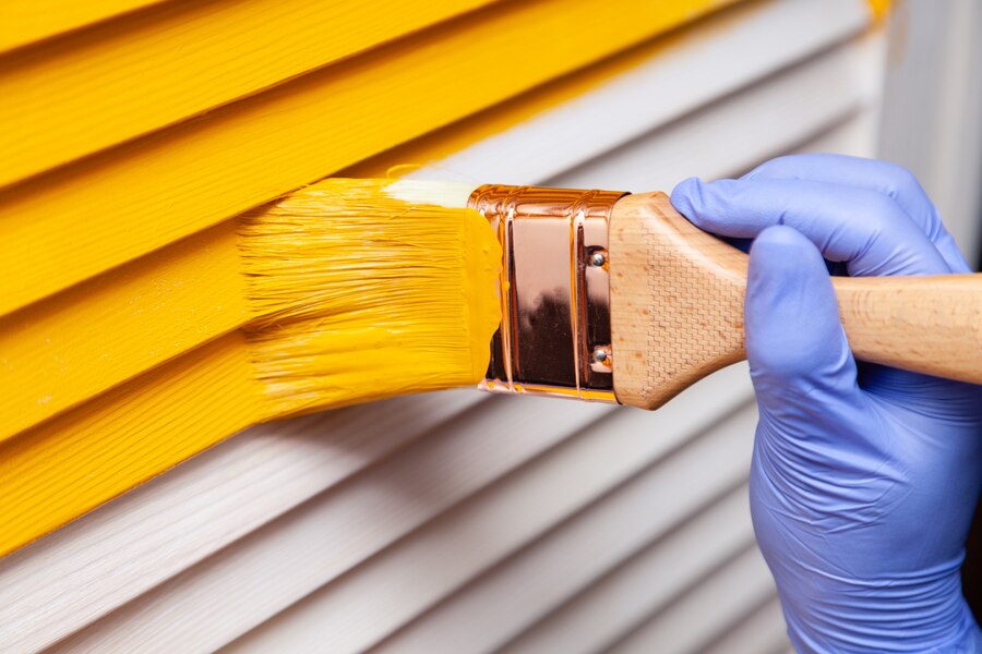 female hand rubber glove with brush painting wooden door with yellow paint